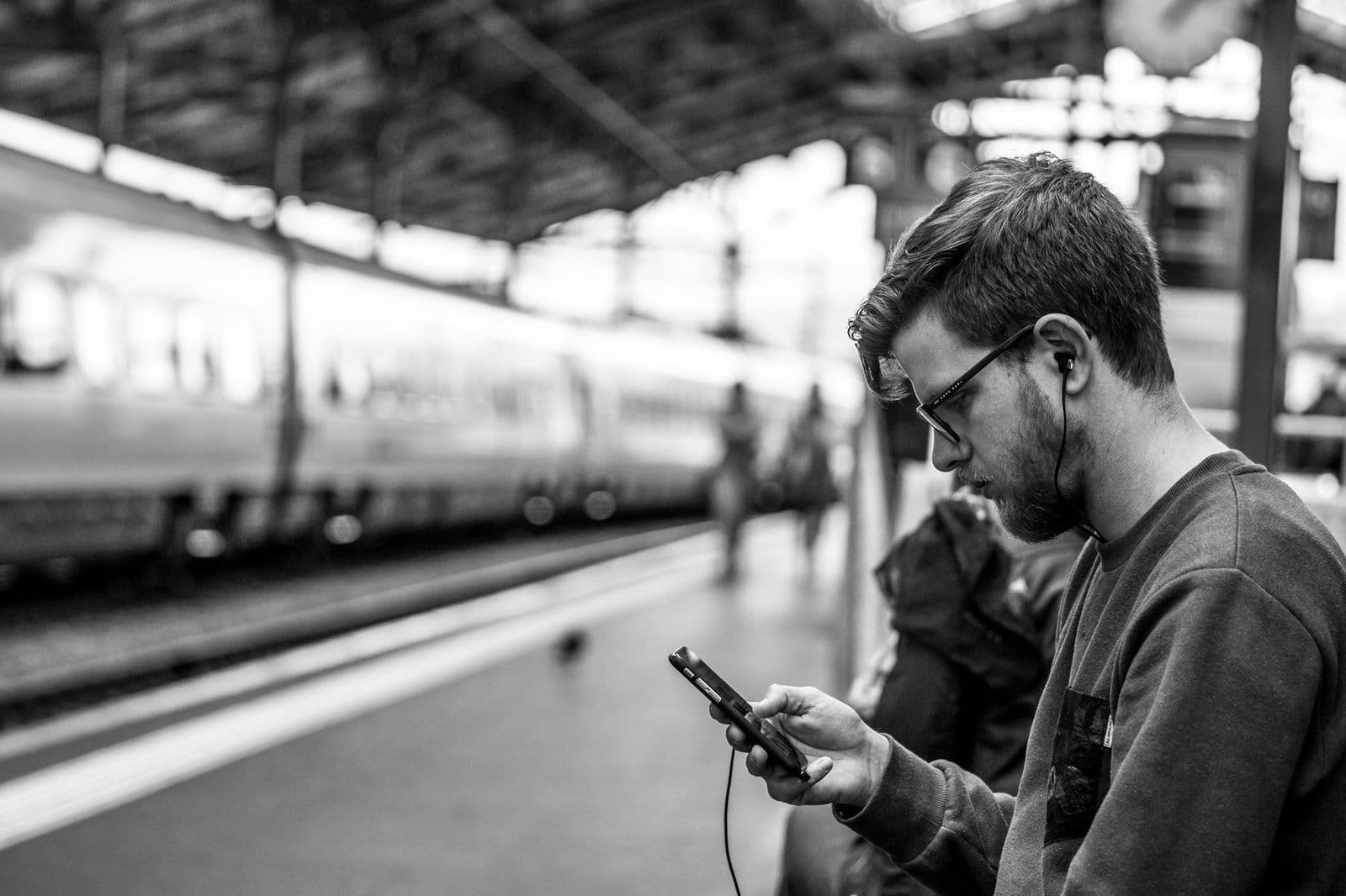 A young person on public transit looking at a phone, one earphone in, waiting out a long voice message